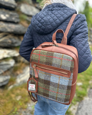 Zu sehen ist ein 30cm großer, cognacfarbener Lerderrucksack mit original Harris Tweed Stoff im highland Schottenkaro.