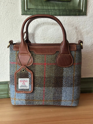 Die Mini Tote ist in Vorderansicht zu sehen. Sie ist vorne aus Harris Tweed® in Kombination mit cognacfarbenen, hellbraunem Leder gearbeitet. Zwei Griffe ermöglichen, die Mini Tote in den Händen zu tragen.
Als Gütesiegel ist das Harris Tweed® Logo auf einem Label angebracht.