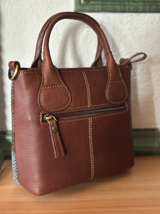 Die Mini Tote ist in Schrägansicht von hinten zu sehen. Die Rückseite ist vollständig aus cognacfarbenen Leder gearbeitet. Die Mini Tote hat hinten zudem ein Reißverschlussfach, um schnell kleinere Gegenstände verstauen zu können.