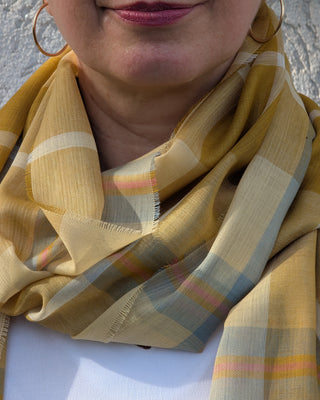 Der feine karierte Merinoschal in den Farben gelb, gold, weiß und hellblau ist als Schlaufe an einem weiblichen Model drapiert.