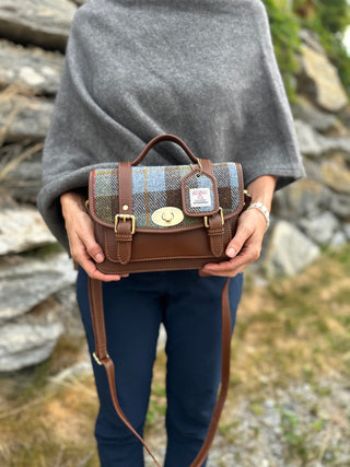 Die Satchel Bag ist im Tageslicht abgelichtet. Farbentreu ist der Harris Tweed und das cognacfarbene Echtleder zu sehen. Die Tasche wird in beiden Händen von einer weiblichen Person gehalten, um das Größenverhältnis zu sehen.