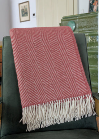 Zu sehen ist eine klassische Herringbone-Decke aus reiner Schurwolle in der Farbe Cranberry. Sie ist über einen Lehnsessel gelegt. 