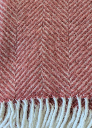 Zu sehen ist eine Detailaufnahme einer klassischen Herringbone-Decke aus reiner Schurwolle in der Farbe Cranberry.