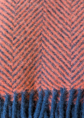 Zu sehen ist eine Detailaufnahme einer klassischen Herringbone-Decke aus reiner Schurwolle in den Farben Flamingo und Marineblau.