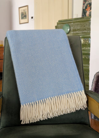Zu sehen ist eine klassische Herringbone-Decke aus reiner Schurwolle in der Farbe Meerblau. Sie ist über einen Lehnsessel gelegt. 