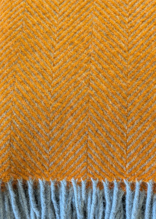 Zu sehen ist eine Detailaufnahme einer klassischen Herringbone-Decke aus reiner Schurwolle in den Farben Orange & Grau.