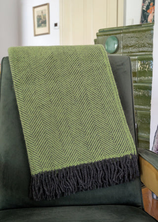 Zu sehen ist eine klassische Herringbone-Decke aus reiner Schurwolle in den Farben Zest & Holzkohle. Sie ist über einen Lehnsessel gelegt. 