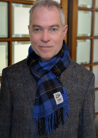 Zu sehen ist ein liegender karierter Wollschal in den Farben Mittelblau und Schwarz mit Akzenten in Rot und Gelb, getragen von einem männlichen Model.