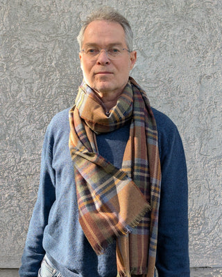 Der fein karierter Schal aus Wolle und Kaschmir in den Farben beige, braun, blau und grün ist an einem männlichen Model als Schlaufe am Hals drapiert. 